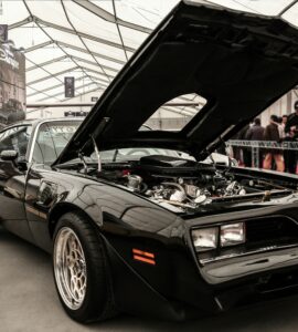 Black 1970s muscle car with its hood raised on display indoors