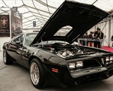 Black 1970s muscle car with its hood raised on display indoors
