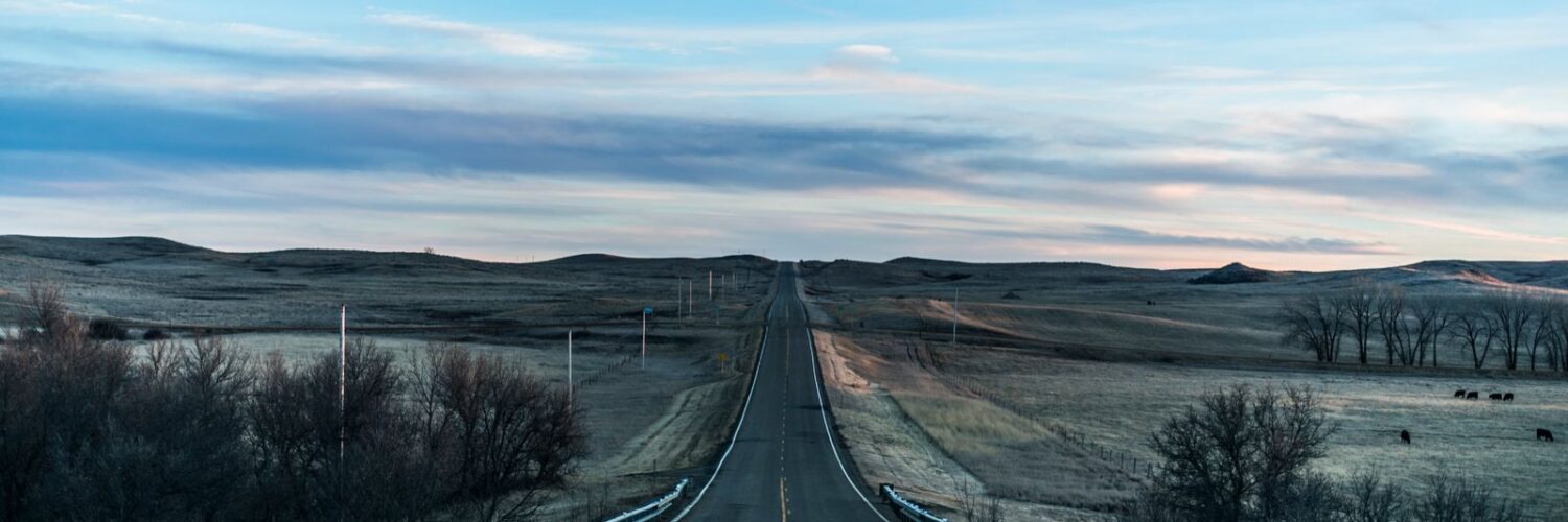 Straight two-lane road running through open prairie under a wide sky