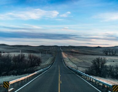Straight two-lane road running through open prairie under a wide sky