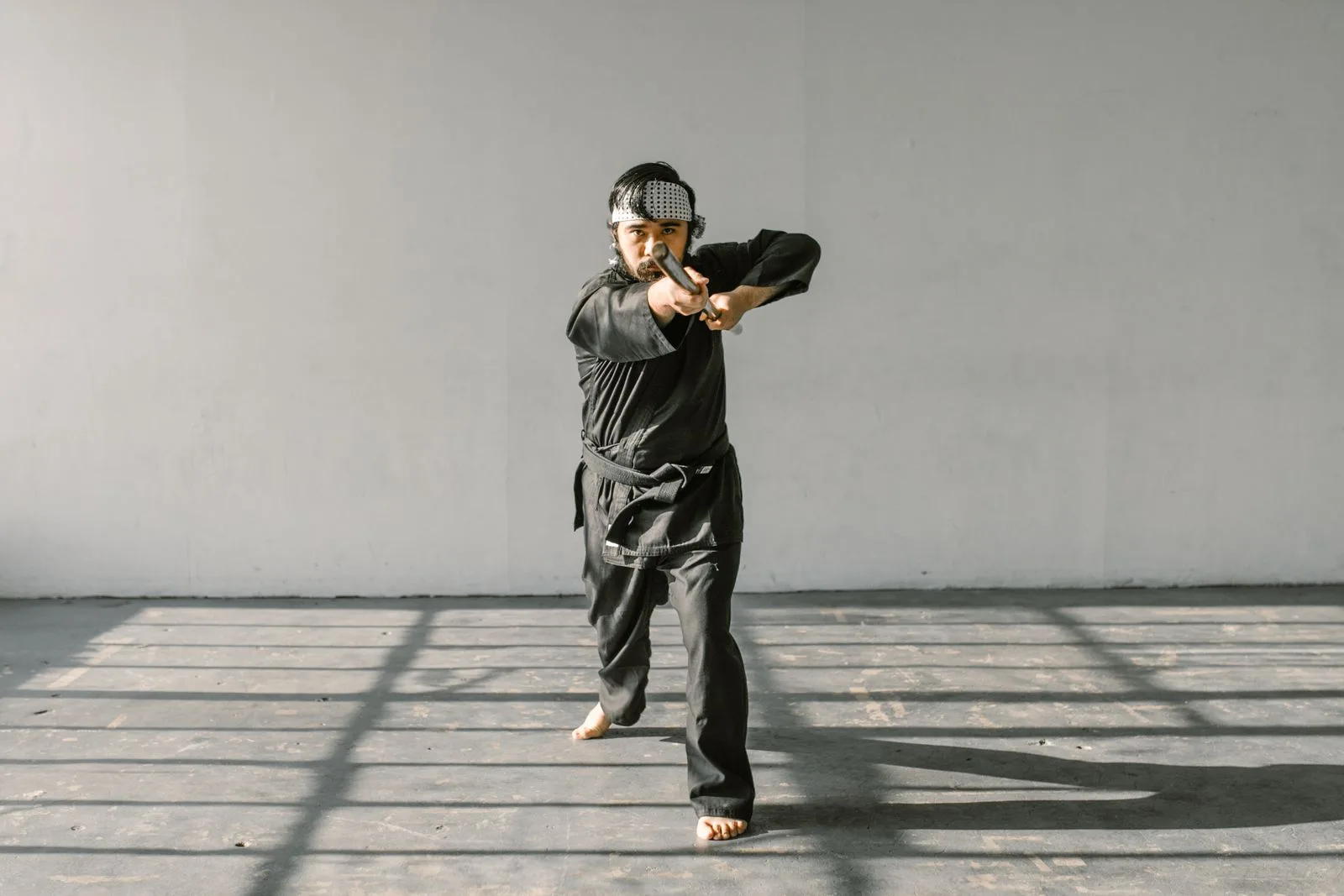 Barefoot martial artist in a black uniform holding a training weapon